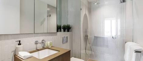 Une salle de bain moderne avec un grand miroir, un lavabo, des toilettes et un espace douche.