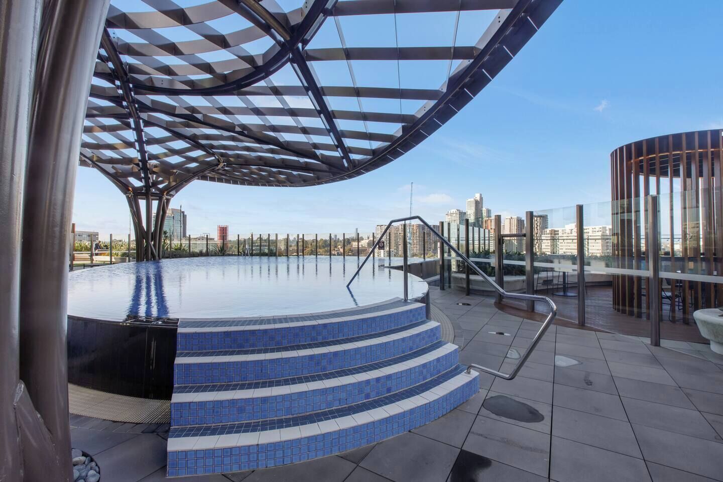 An outdoor infinity pool with a modern architectural design, a glass railing, and a cityscape view in the background.