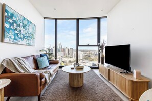 A modern living room with a large window, a leather sofa, a coffee table, and a flat-screen TV. - Southbank Sojourn Resort Comfort and Skyline Views (Southbank)