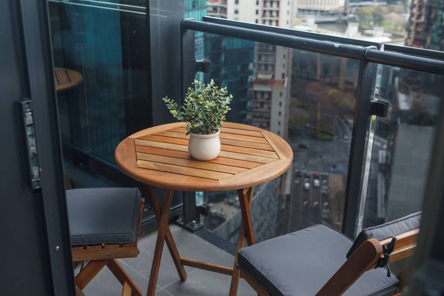 A balcony with a round wooden table, a potted plant, and two chairs.