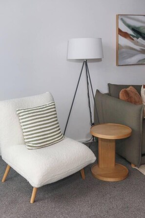 A room with a white armchair, a round wooden side table, a floor lamp, and a green sofa with cushions. - Urban Calm Tranquil Retreat by Yarra River and Crown (Southbank)