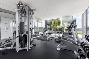 A modern gym with various exercise equipment, large windows, and a view of the city. - Batman Hideout Modern Parkside Escape with Gym (West Melbourne)