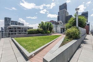 A rooftop garden with a paved walkway, surrounded by modern buildings and a clear sky. - Batman Hideout Modern Parkside Escape with Gym (West Melbourne)