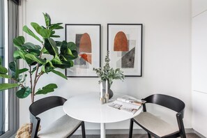 A room with a round white table, two black chairs, a potted plant, and two framed abstract artworks on the wall. - Batman Hideout Modern Parkside Escape with Gym (West Melbourne)