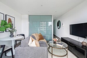 A modern living room with a grey sofa, a round coffee table, a flat-screen TV, and a glass partition wall. - Batman Hideout Modern Parkside Escape with Gym (West Melbourne)
