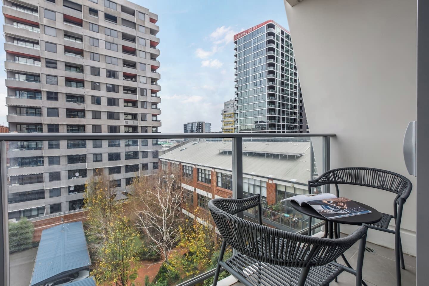 Un balcón con mesa y sillas, con vista a un paisaje urbano con edificios altos.