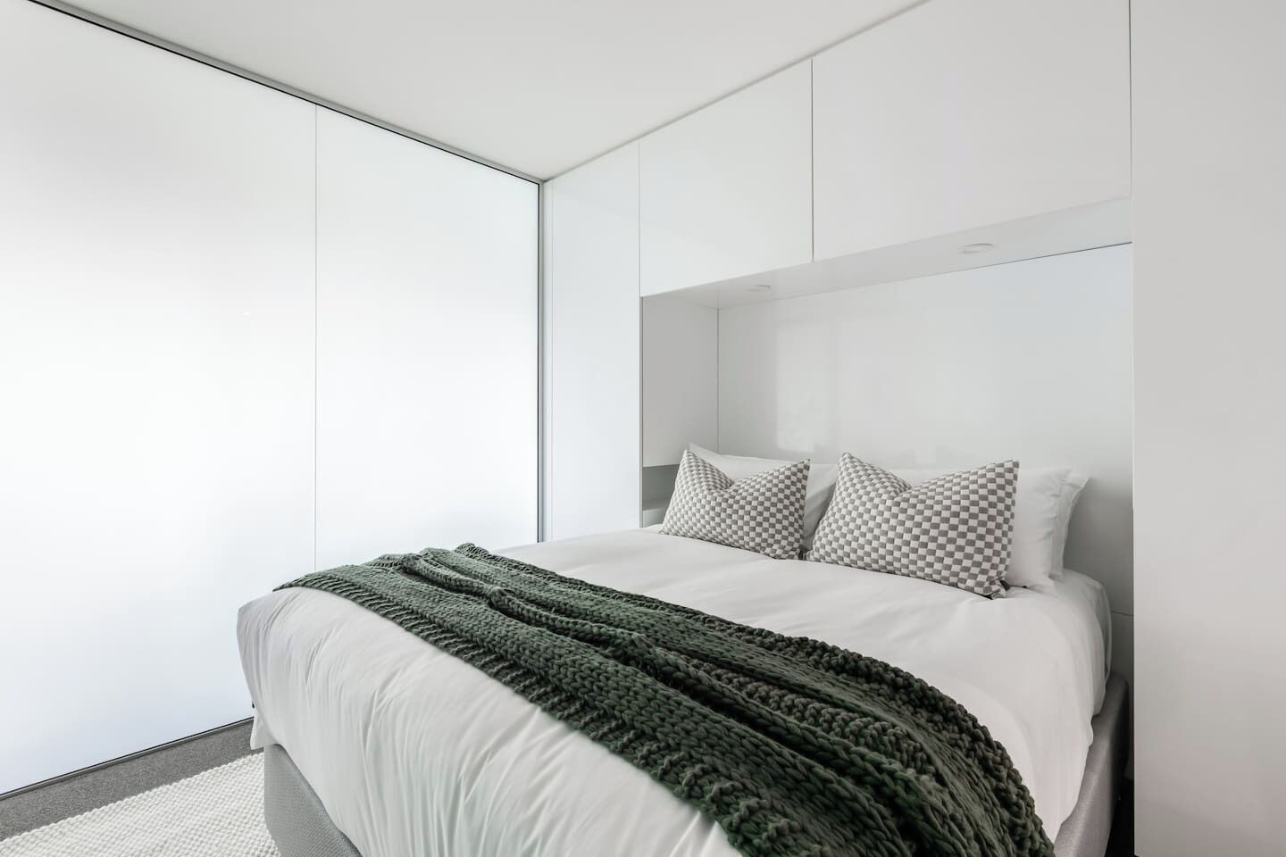 A modern bedroom with a bed, pillows, and a green knitted throw.