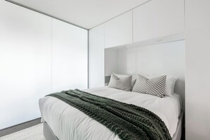 Ein modernes Schlafzimmer mit einem Bett, Kissen und einer grünen Strickdecke.
