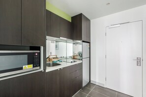 A modern kitchen with dark cabinetry, a microwave, a refrigerator, and a sink. - Batman Hideout Modern Parkside Escape with Gym (West Melbourne)