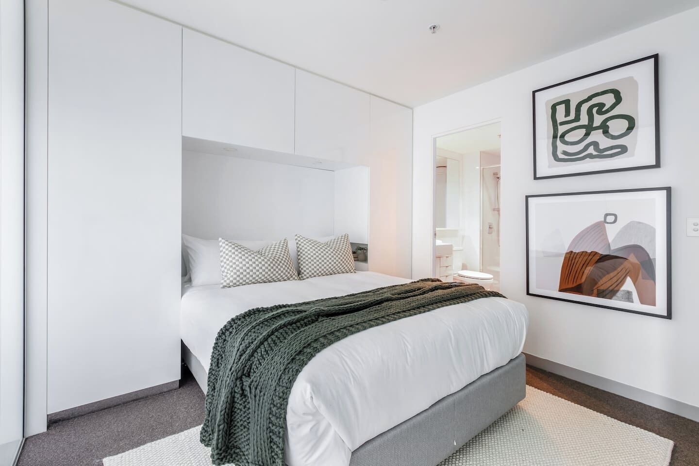 Un dormitorio moderno con una cama, un armario y dos obras de arte enmarcadas en la pared.