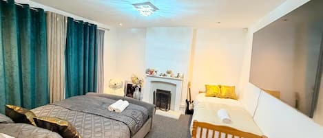 A hotel room with a large bed, a smaller bed, a fireplace, and a TV on the wall.