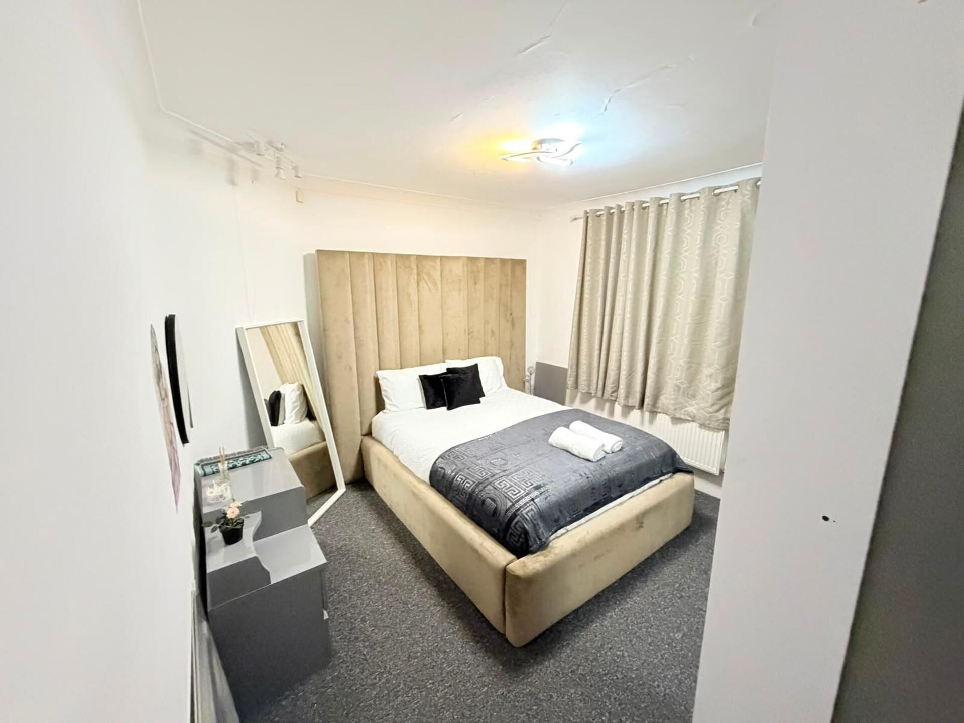 Ein Hotelzimmer mit Bett, Nachttisch, Spiegel, Fenster mit Vorhängen und einer Lampe.