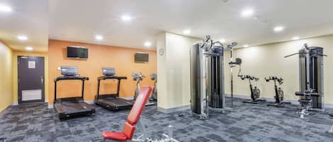 Une salle de sport équipée de tapis de course, d’un banc rouge et de divers appareils d’exercice.