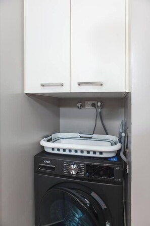 Un appareil compact combinant lave-linge et sèche-linge, doté d’un panneau de commande situé sous un meuble blanc.