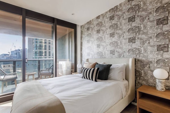 Un dormitorio con una cama grande, vistas de la ciudad y un balcón con sillas.