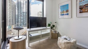 A modern living room with a large TV, a round table, a plant, and a framed picture on the wall. - Urban Cocoon Cosy Riverside Pad with Pool and Sauna (Southbank)