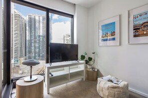 Ein modernes Wohnzimmer mit großem Fernseher, rundem Tisch, einer Pflanze und einem gerahmten Bild an der Wand.