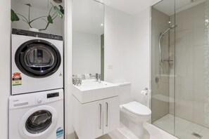 A compact bathroom with a washing machine, a toilet, and a glass-enclosed shower. - Urban Cocoon Cosy Riverside Pad with Pool and Sauna (Southbank)