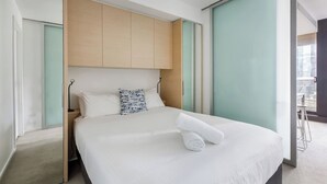 A modern hotel room with a large bed, a wooden headboard, and a view of the city. - Urban Cocoon Cosy Riverside Pad with Pool and Sauna (Southbank)