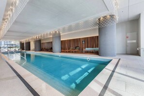 An indoor swimming pool with a tiled floor, lounge chairs, and a wooden wall. - Urban Cocoon Cosy Riverside Pad with Pool and Sauna (Southbank)