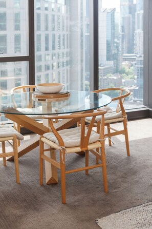 A modern dining area with a glass table and wooden chairs, overlooking a cityscape through large windows. - Yarra Vista Riverside City Escape by Crown Casino (Southbank)