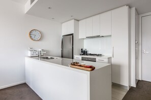 Eine moderne Küche mit weißen Schränken, einem Edelstahlkühlschrank, einem eingebauten Ofen und einer Wanduhr.