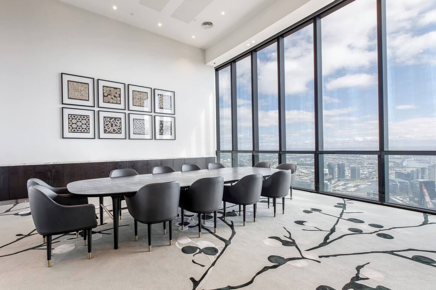 Une salle de conférence dotée d’une grande table et de chaises, avec des œuvres d’art encadrées accrochées au mur et une vue sur la ville grâce à de grandes fenêtres.