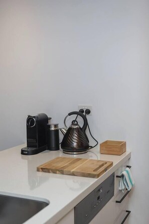 Een keuken met een waterkoker, een koffiezetapparaat en een houten snijplank op het aanrecht.