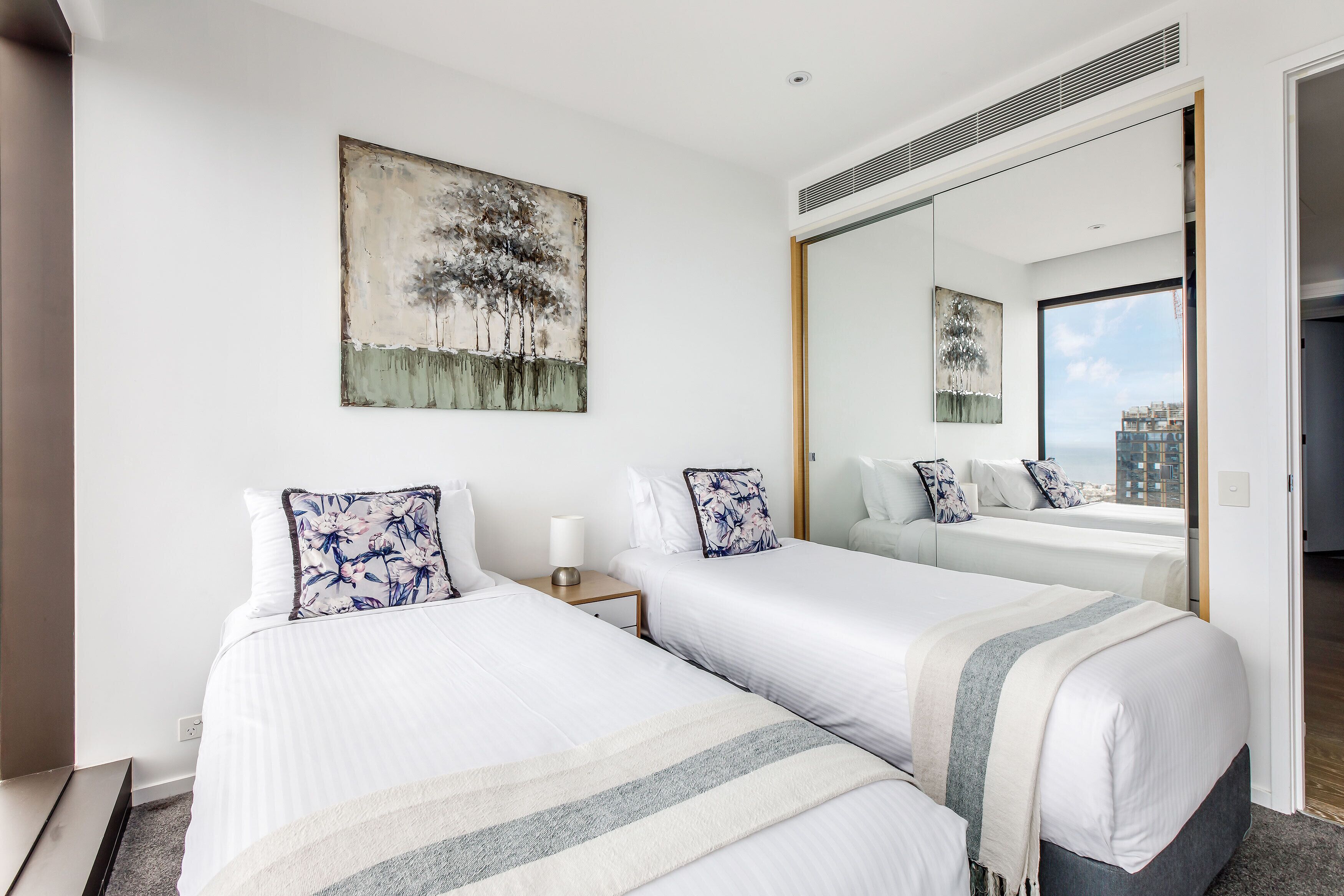 A hotel room with two beds, a large mirror, and a painting on the wall.