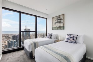 Ett hotellrum med två sängar, ett stort fönster med utsikt över staden och en tavla på väggen.