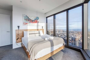 Een moderne slaapkamer met een groot bed, stadszicht en een opvallend kunstwerk aan de muur.
