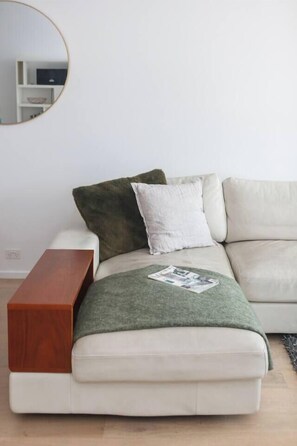 Un salon moderne avec un canapé, une table d’appoint en bois et un miroir rond accroché au mur.