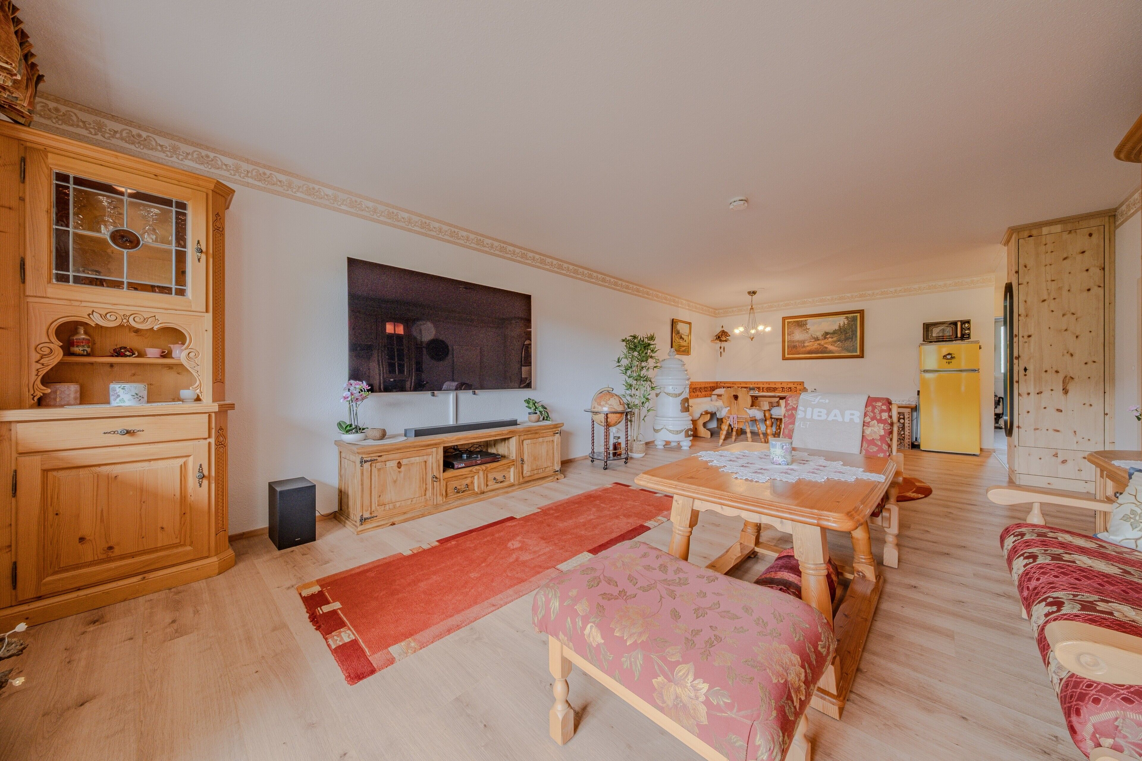 Ein Wohnzimmer mit einer Holzkommode, einem Fernseher, einem Esstisch und einem Sofa.