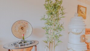 A round table with a globe and a bottle, a tall bamboo plant in a vase, and a white decorative object with a small door. - View of Todtmoos with a Panoramic Balcony – My SWH (Todtmoos)