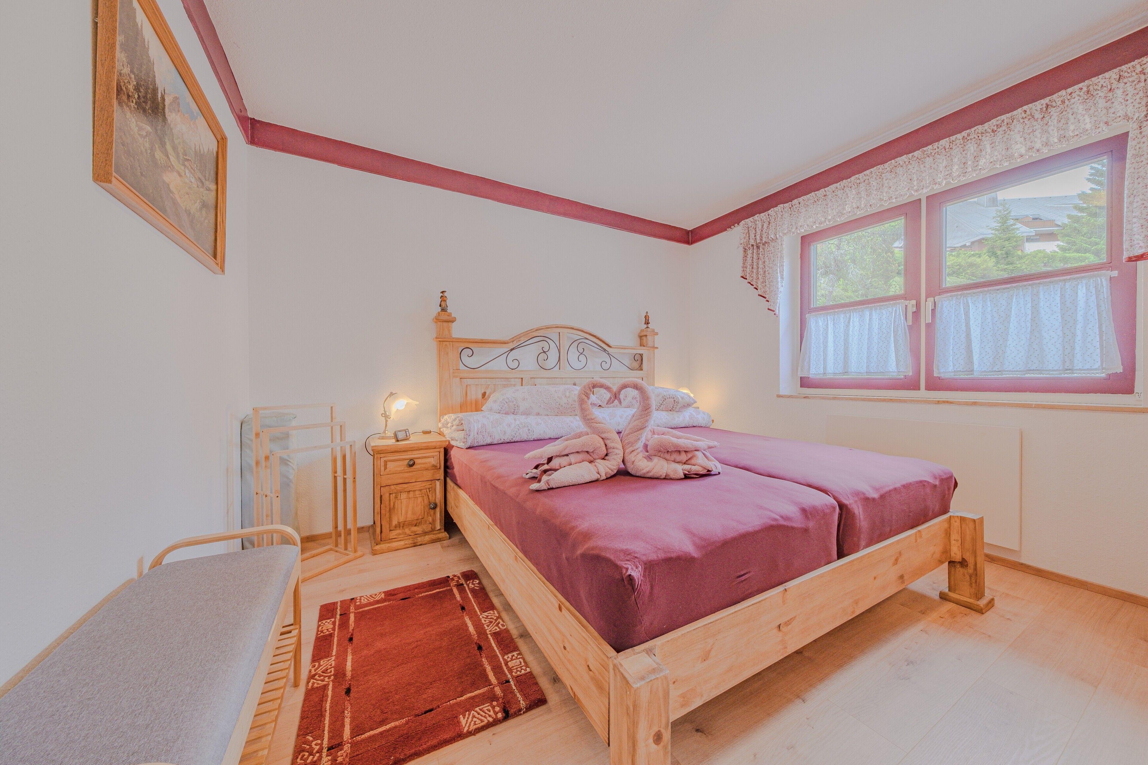 Quarto com cama de madeira, mesa de cabeceira e um quadro na parede, além de uma janela com cortinas.
