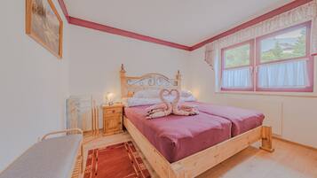 Quarto com cama de madeira, mesa de cabeceira e um quadro na parede, além de uma janela com cortinas.