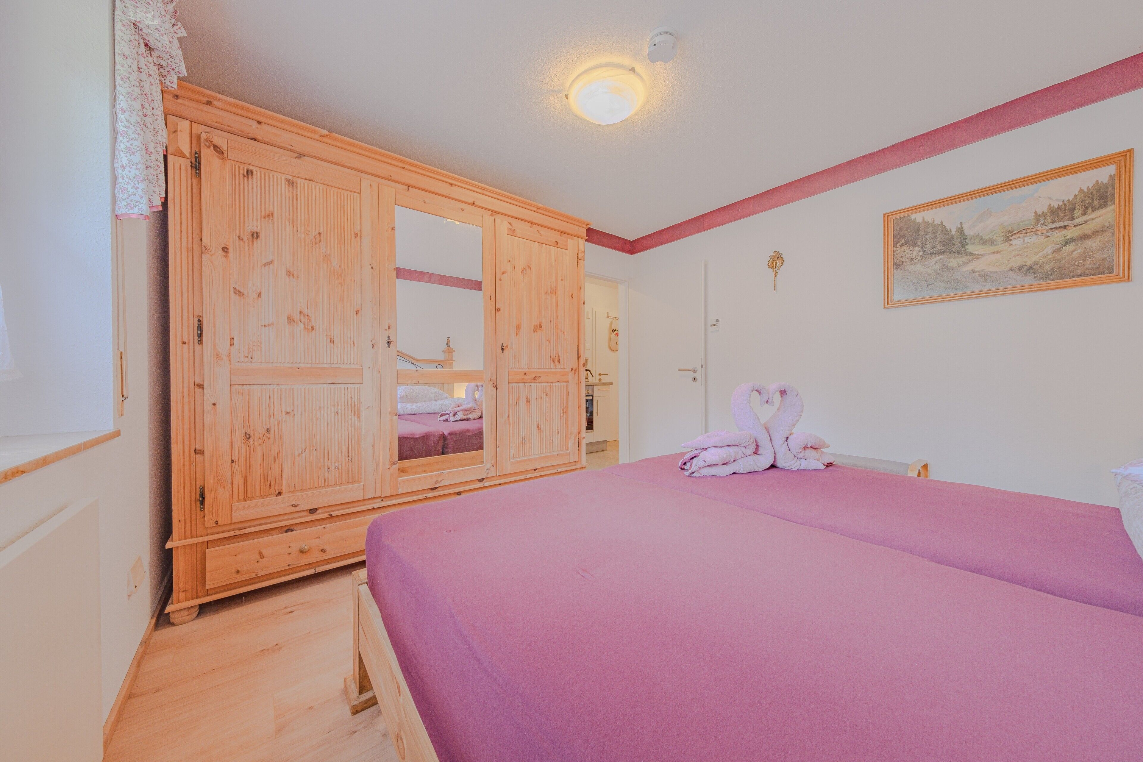 Ein Zimmer mit großem Holzschrank, einem Bett mit rosa Bettwäsche und einem Gemälde an der Wand.