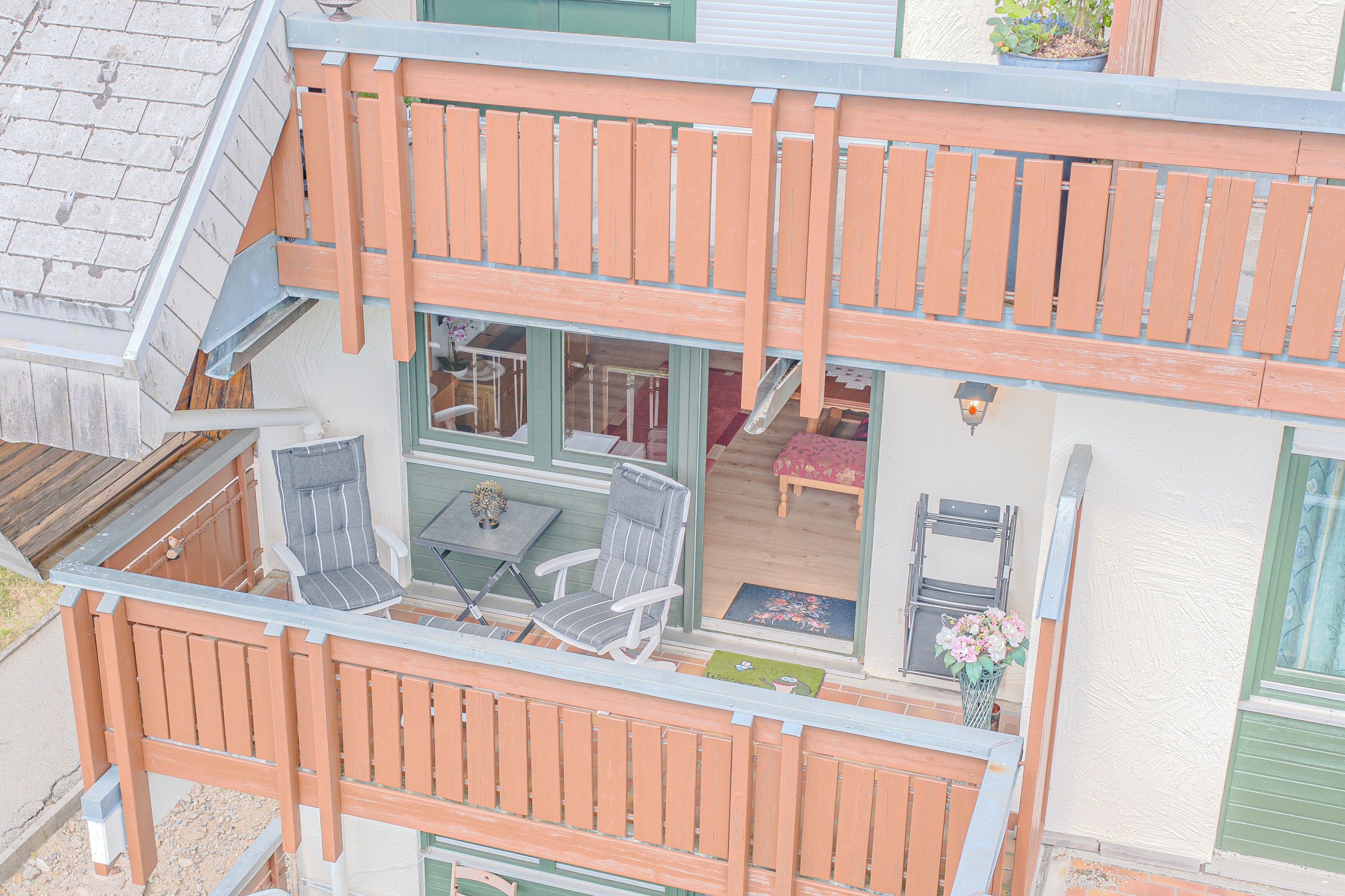 Ein zweistöckiges Haus mit einem Balkon, einem Essbereich mit Stühlen und einem Tisch sowie einer sichtbaren Treppe.