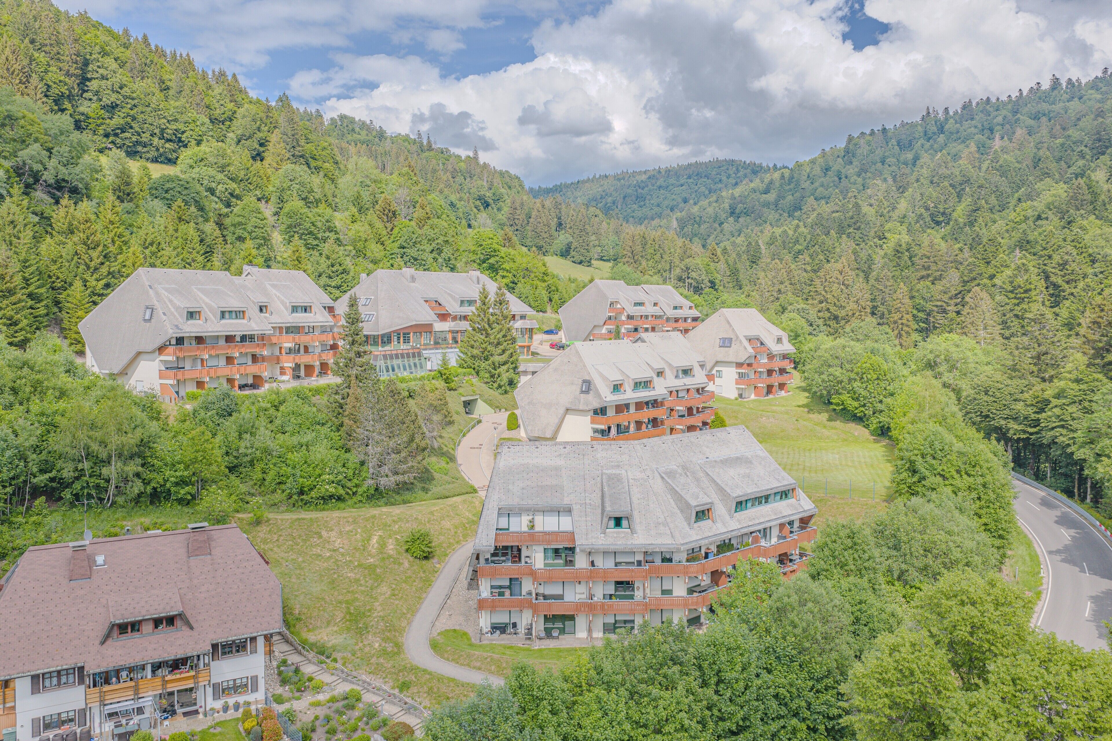 Ein Wohngebiet mit mehreren zweistöckigen Gebäuden, die Balkone haben, vor einer hügeligen, bewaldeten Landschaft.