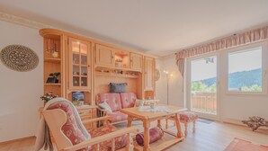 A cozy living room with a wooden sofa, a wooden dining table, and a view of a balcony. - View of Todtmoos with a Panoramic Balcony – My SWH (Todtmoos)