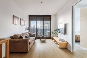 A modern living room with a sofa, a coffee table, and a TV on a wall. - Evara Resort Style Living by Yarra River and Crown (Southbank)
