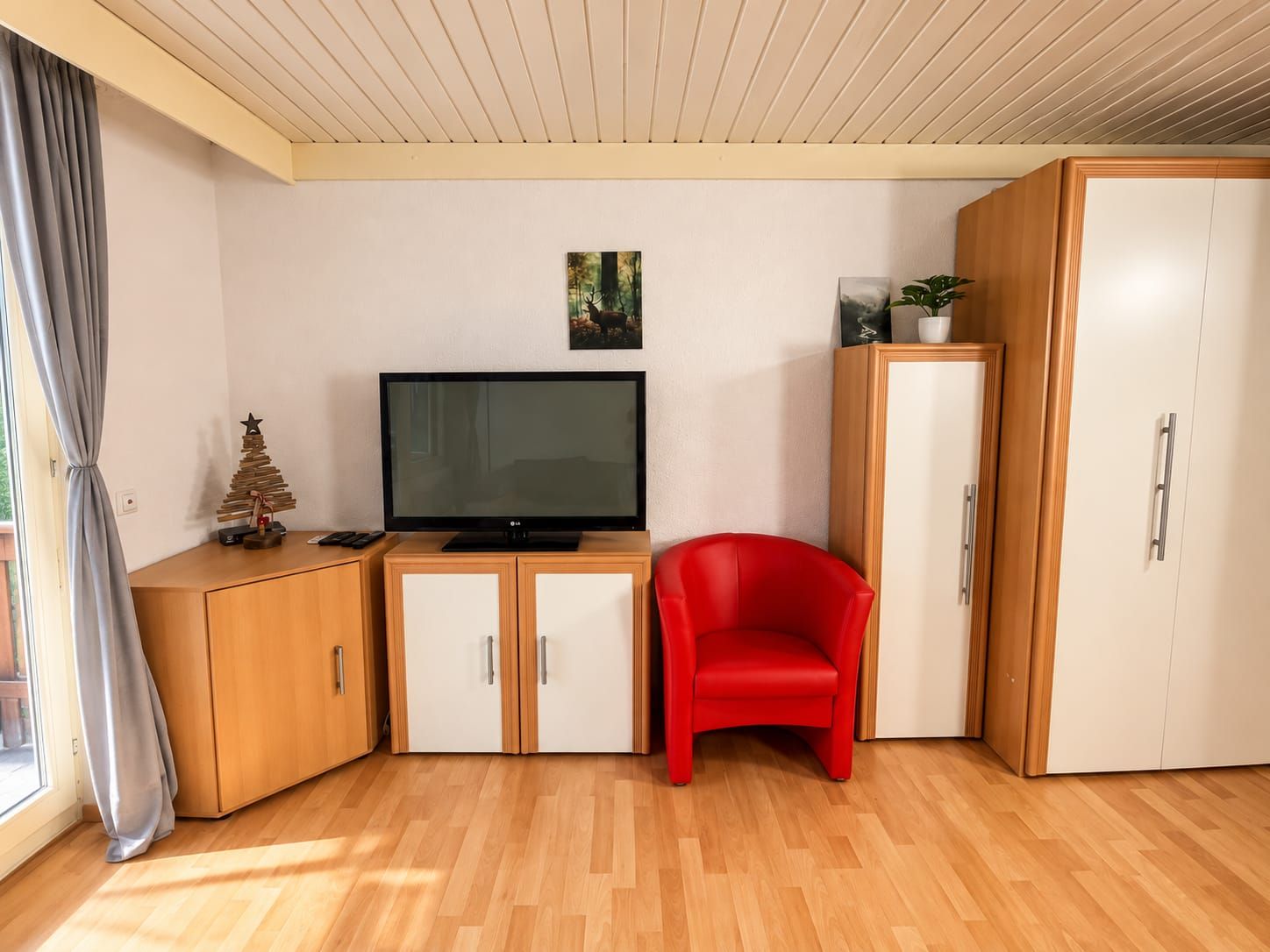 Une pièce avec un téléviseur posé sur un meuble en bois, une chaise rouge et une armoire.