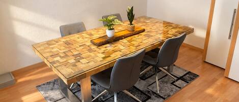 A dining table with a woven top, two chairs, a potted plant, and a hanging light fixture.