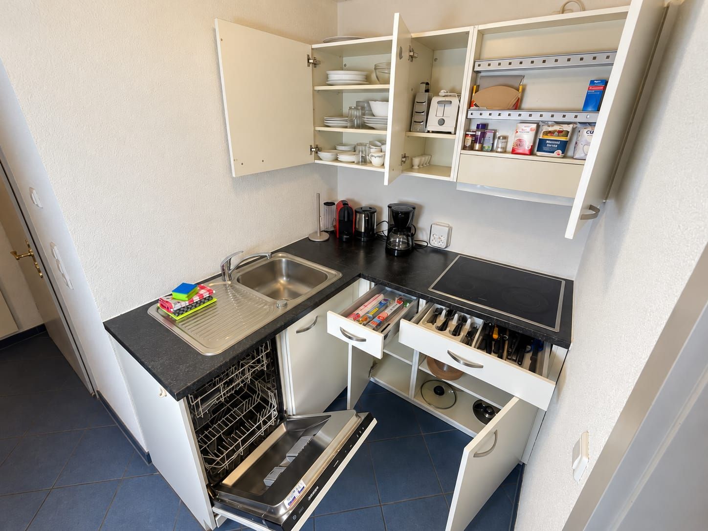 Une petite cuisine équipée comprenant un lave-vaisselle intégré, un évier et un plan de travail avec des tiroirs de rangement.