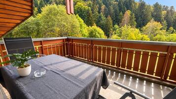 Un balcon avec une table et des chaises, un pot de fleurs et une vue sur une colline boisée.