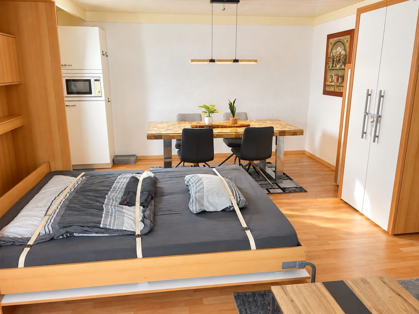 Ein gemütliches Schlafzimmer mit Bett, Holzschrank, einer Küchenzeile und einer Essecke mit Stühlen und Tisch.