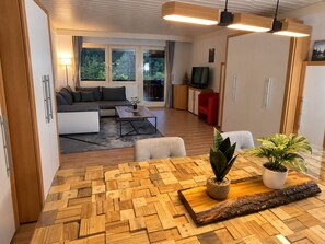 A modern living room with a sofa, coffee table, and a dining area with a wooden table and chairs. - Pine Forest Bliss – A Wonderful Vacation with a Stunning Balcony View – My Little Black Forest Cottage (Todtmoos)