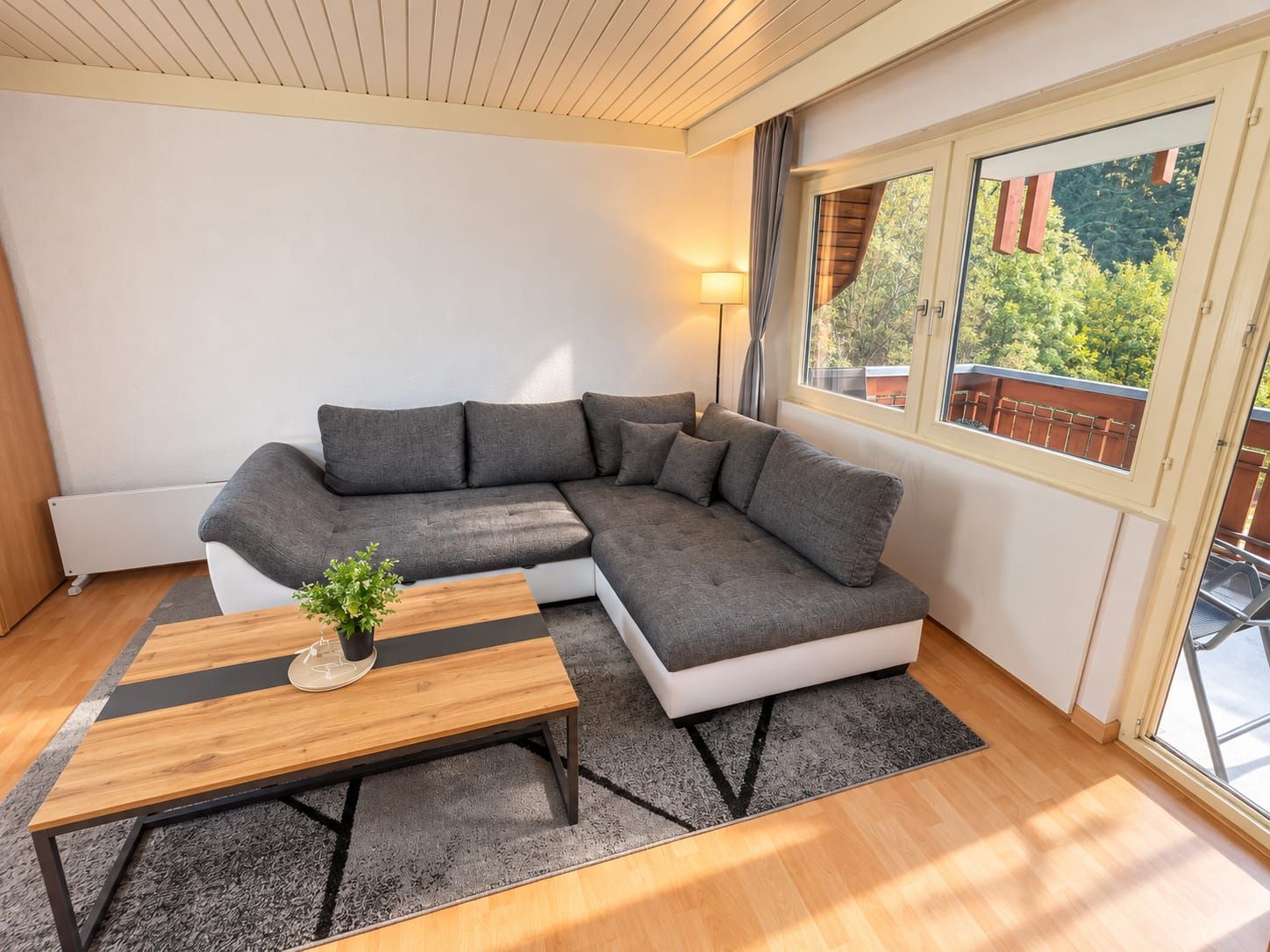 A modern living room with a sectional sofa, a wooden coffee table, and a view of greenery through a window.