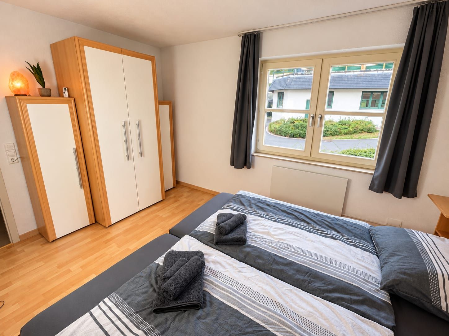 Une chambre à coucher avec un lit, une armoire, une fenêtre avec des rideaux et une vue sur l’extérieur.