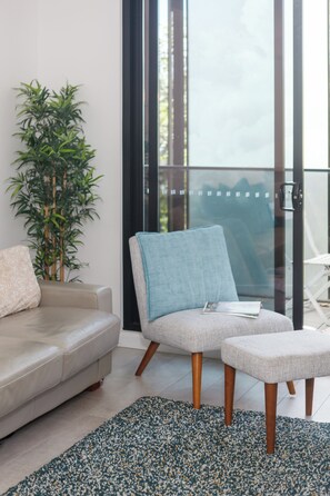 A modern living room with a sofa, a blue armchair, and a matching ottoman. A large potted plant is in the corner, and there is a glass door leading to a balcony. - Vyra at Arden Park Minutes to Dining Shops and CBD (North Melbourne)